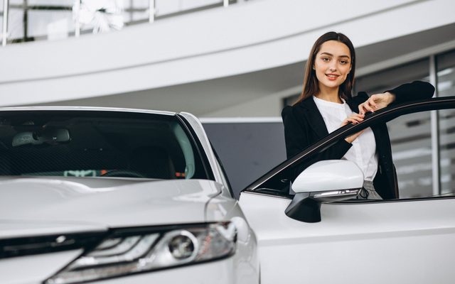A woman standing at the open door of a white car