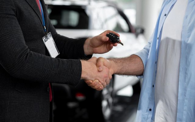 A salesperson handing car keys to a buyer beside a car